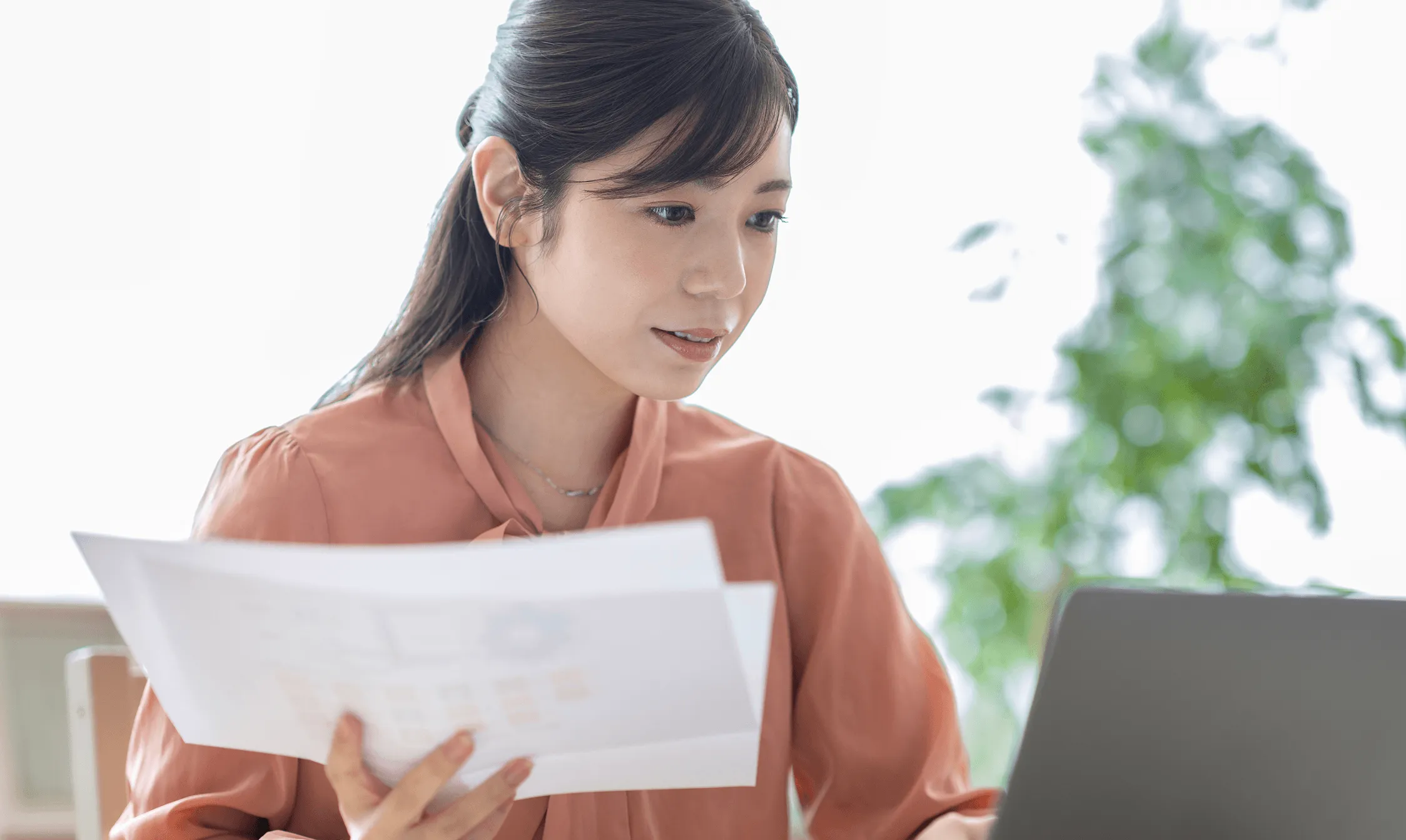 書類とノートパソコンを見ながら作業する女性