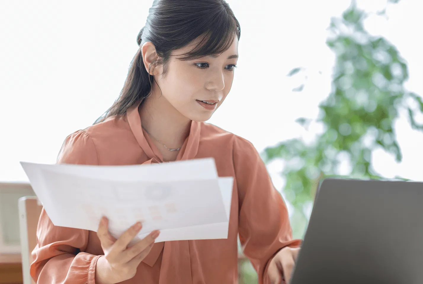 書類とノートパソコンを見ながら作業する女性