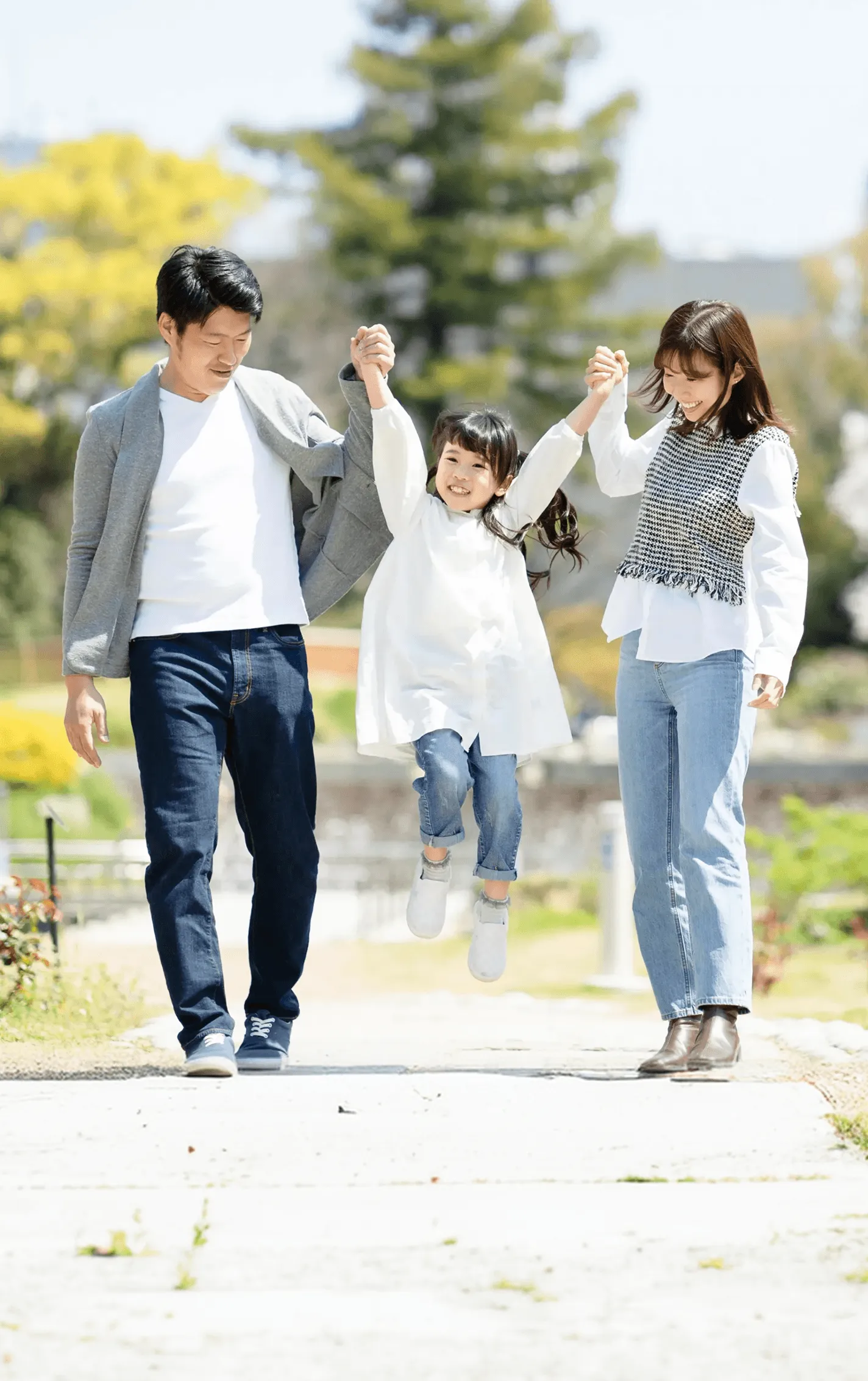 公園で両手を引かれ、跳ぶように歩く女の子と両親