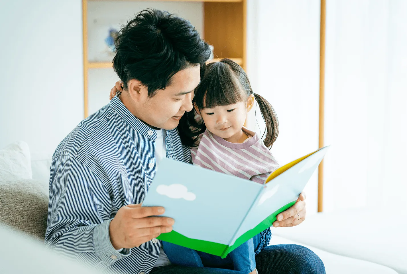 絵本を開いて読む父親と、膝の上の幼い女の子